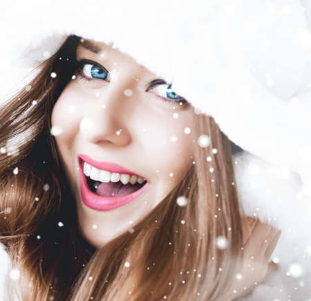 Christmas and winter holiday portrait of young woman in white hooded fur coat, snow on blue background, fashion and lifestyle campaignの写真素材
