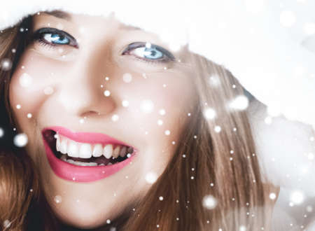 Christmas and winter holiday portrait of young woman in white hooded fur coat, snow on blue background, fashion and lifestyle campaignの写真素材