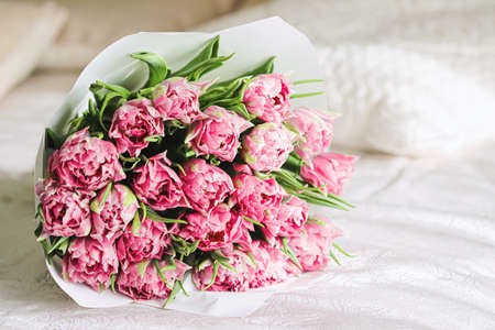 Romantic bouquet of pink tulips on bed in bedroom, holiday gift conceptの写真素材