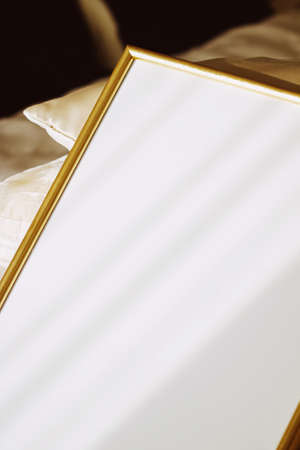 Golden frame for art, poster or photo on bed at sunset, home decor conceptの写真素材