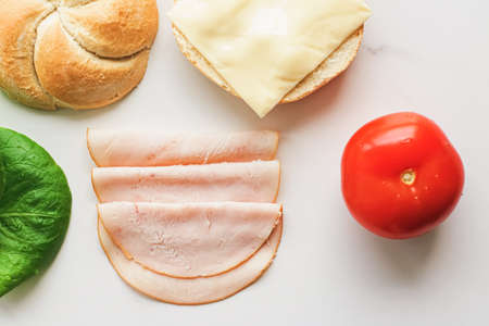 Food products and ingredients for making sandwich. Ham, cheese, burger bun, lettuce, cucumber and tomato as recipe flatlay on marble kitchen table backgroundの写真素材