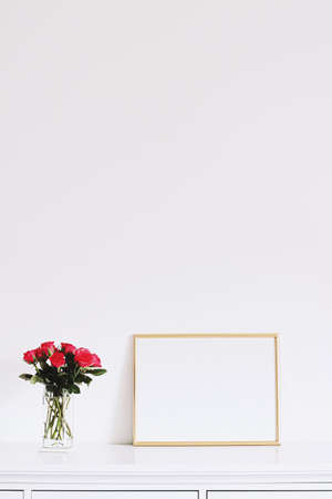 Golden horizontal frame and bouquet of rose flowers on white furniture, luxury home decor and design...
