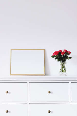 Golden horizontal frame and bouquet of rose flowers on white furniture, luxury home decor and design...