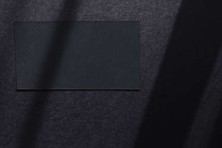 Black business card on dark flatlay background and sunlight shadows, luxury branding flat lay and...