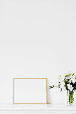Golden horizontal frame and bouquet of fresh flowers on white furniture, luxury home decor and design for mockup creationの写真素材