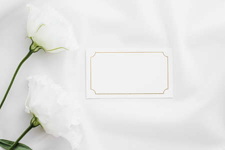 Wedding invitation or gift card and white rose flowers on silk fabric as bridal flatlay background,...
