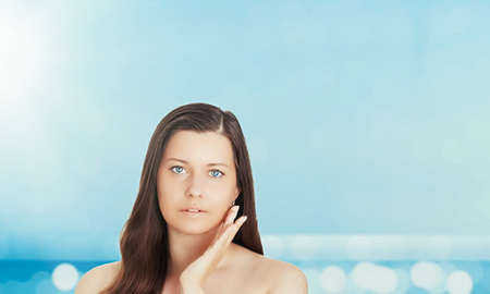 Skincare and sun protection in summer. Portrait of a beautiful young suntanned woman, blue sea and sky on background, beauty, wellness and travel conceptの写真素材