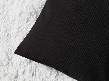 Black cushion throw pillow on white fluffy plaid blanket as flat lay background, bedroom top view...