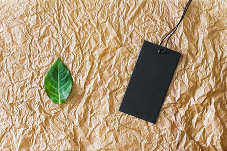 Grean leaf and black price tag on recycled material as flatlay background, sustainable fashion and brand label conceptの写真素材