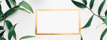 Blank white and gold card, green leaves on white background as botanical frame flatlay, wedding...