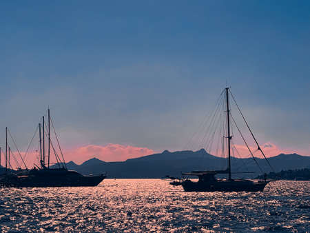 Tranquil seascape and coastal nature concept. Sea, boats, mountains and blue sky over horizon at sunsetの写真素材