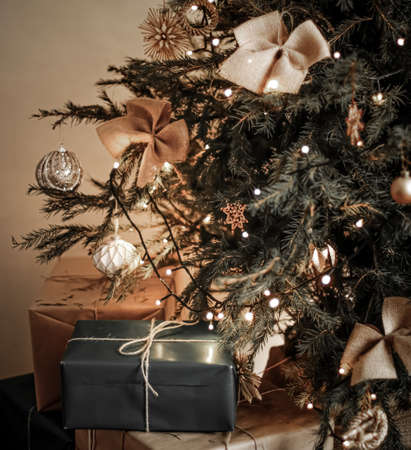 Christmas holiday delivery and sustainable gifts concept. Black gift boxes wrapped in eco-friendly packaging with recycled paper under decorated xmas treeの写真素材