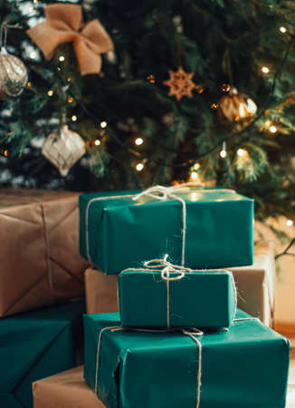 Christmas holiday delivery and sustainable gifts concept. Green blue gift boxes wrapped in eco-friendly packaging with recycled paper under decorated xmas treeの写真素材