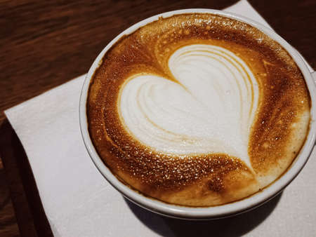Coffee break and romantic mood concept. Cup of caramel cappuccino with heart shaped foam art made of...