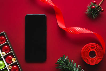 Christmas phone app and holiday message concept. Smartphone with blank black screen and xmas decoration on red background as flat lay mockup designの写真素材