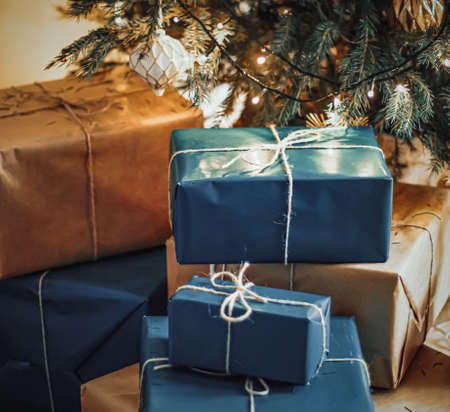 Christmas holiday delivery and sustainable gifts concept. Navy blue gift boxes wrapped in eco-friendly packaging with recycled paper under decorated xmas treeの写真素材