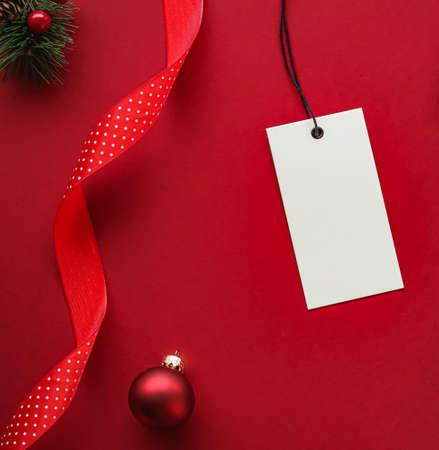 Christmas sale and holiday fashion design concept. Blank clothing tag and xmas decoration and ornaments on red paper background as flatlay mockupの写真素材