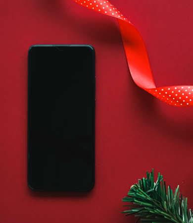 Christmas phone app and holiday message concept. Smartphone with blank black screen and xmas decoration on red background as flat lay mockup designの写真素材