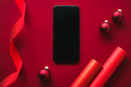 Christmas phone app and holiday message concept. Smartphone with blank black screen and xmas decoration on red background as flat lay mockup designの写真素材