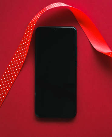 Christmas phone app and holiday message concept. Smartphone with blank black screen and xmas decoration on red background as flat lay mockup designの写真素材