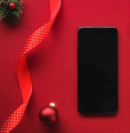 Christmas phone app and holiday message concept. Smartphone with blank black screen and xmas decoration on red background as flat lay mockup designの写真素材