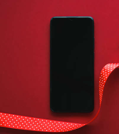 Christmas phone app and holiday message concept. Smartphone with blank black screen and xmas decoration on red background as flat lay mockup designの写真素材