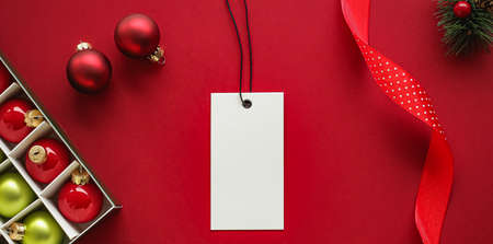 Christmas sale and holiday fashion design concept. Blank clothing tag and xmas decoration and ornaments on red paper background as flatlay mockupの写真素材