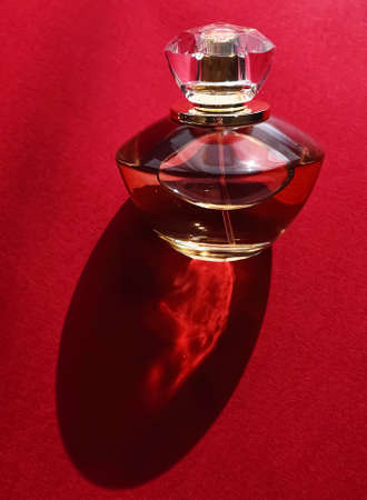 Flacon of perfume made of glass and gold on red backgroundの写真素材
