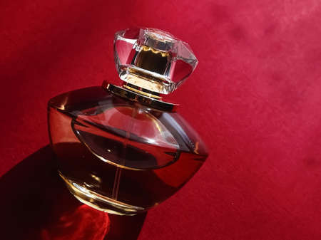 Flacon of perfume made of glass and gold on red background