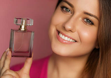 Perfume, beauty product and cosmetics model face portrait on pink background, beautiful woman holding fragrance bottle with floral feminine scent, fashion and makeup conceptの写真素材