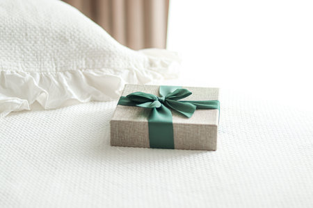 Holiday present and luxury online shopping delivery, wrapped linen gift box with green ribbon on bed in bedroom, chic countryside style, close-upの写真素材