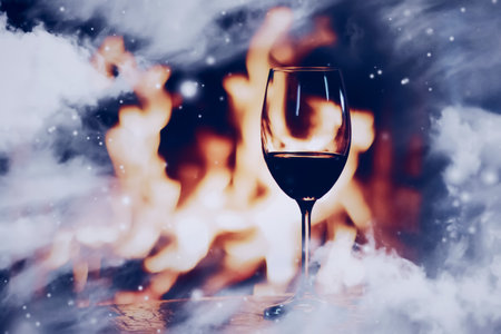 Winter atmosphere and Christmas holiday time, glass of wine in front of fireplace covered with snowy effect on window glass, holidays backgroundsの写真素材