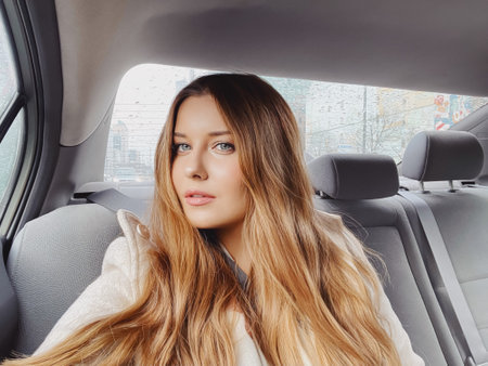 Young woman with long hair, wavy hairstyle in the car or taxi cab as passenger, exploring the city, transport and travel ideaの写真素材