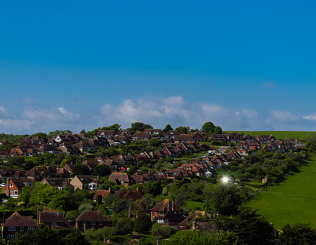Rural residential houses built on a sunny hillside with vibrant green fields and blue sky. East Sussex countryside, Englandの写真素材