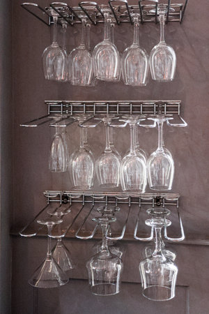 Clear crystal wine glasses, cocktail glasses, and martini glasses hanging on metal bar racks, clean and organizedの写真素材