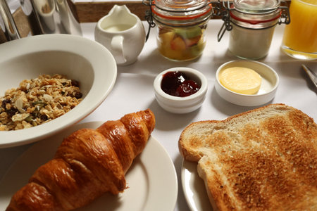 Continental breakfast spread with croissant, toast, granola, fruit, jam, butter, and orange juice....