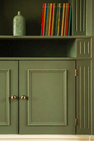 Charming green wooden cabinet adorned with an array of colorful books and a delicate ceramic vase, bringing a sense of warmth and order to the home decorの写真素材