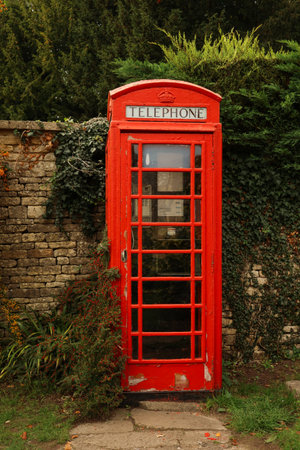 British red telephone box, an iconic symbol, standing beside an old stone wall with a vintage,...