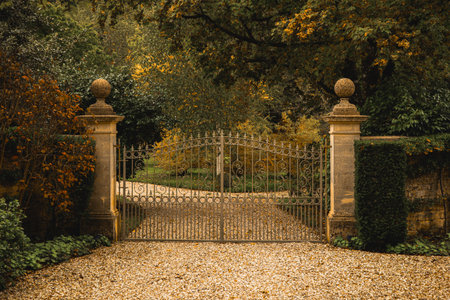Ornate iron gates with stone pillars and a gravel driveway in a peaceful autumn setting. Cotswolds countryside, Englandの写真素材