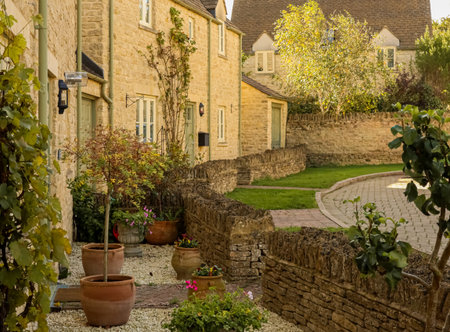 Quaint English village street featuring traditional stone houses, dry stone walls, and green gardens. Cotswolds countryside, Englandの写真素材