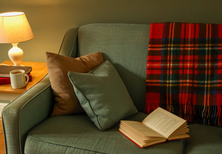 Sofa with pillows, a plaid blanket, an open book, and a coffee mug creating a warm, cozy, and relaxing home sceneの写真素材
