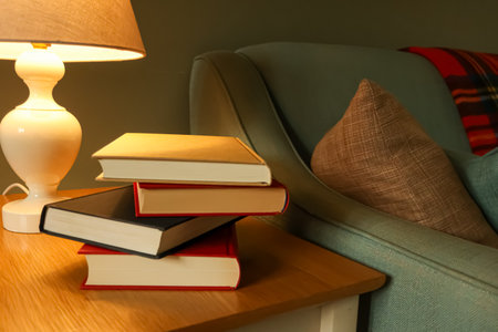 Books resting on a table by a comfortable armchair and warm lamp, creating a peaceful, inviting...
