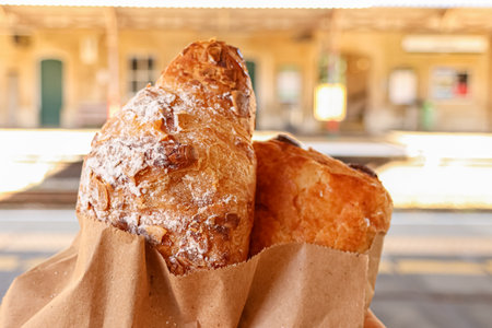 Holding fresh sweet pastries, including an almond croissant, in paper bags, offering a quick...