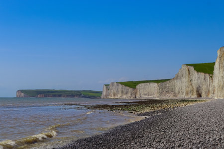 The Seven Sisters cliffs, towering above the pebbled shoreline of the English Channel, present a...