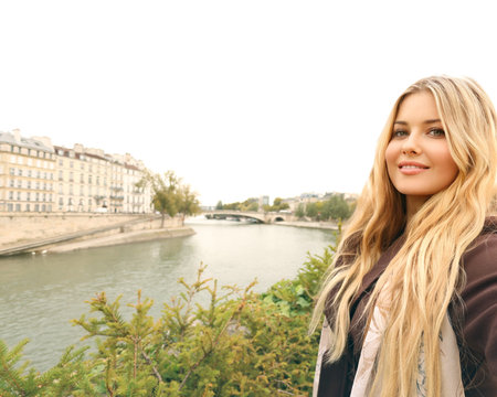 Blonde woman traveling in Paris, overlooking the Seine River and historic buildings, enjoying a city vacationの写真素材