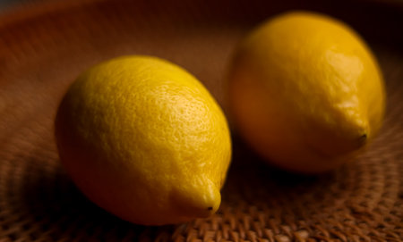 Two ripe yellow lemons displaying their textured rinds on a rustic brown woven wicker surface, emphasizing freshness and natural foodの写真素材