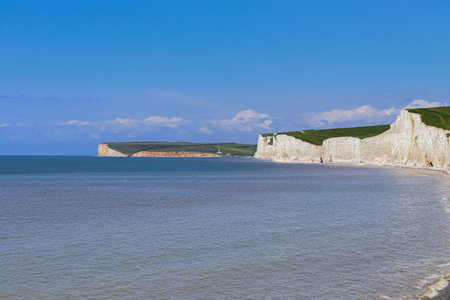 Iconic Seven Sisters white chalk cliffs rising from the calm English Channel water under a clear...