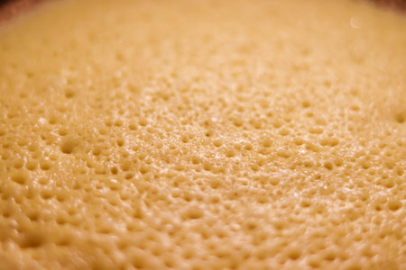 Pancake batter cooking in a pan with many bubbles creating a porous texture, preparing a delicious homemade breakfastの写真素材