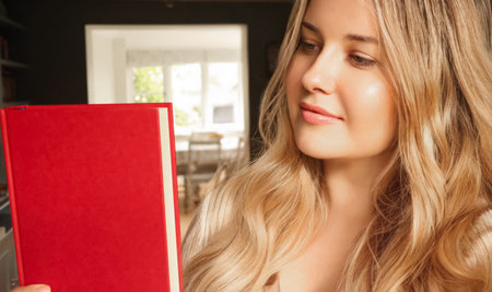 Young woman intently reading a red book, focusing on literature and acquiring knowledge for education and learningの写真素材