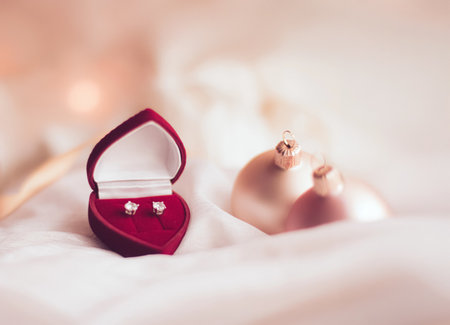 Heart shaped jewelry box holding shiny diamond earrings against a soft background with festive Christmas decorationsの写真素材